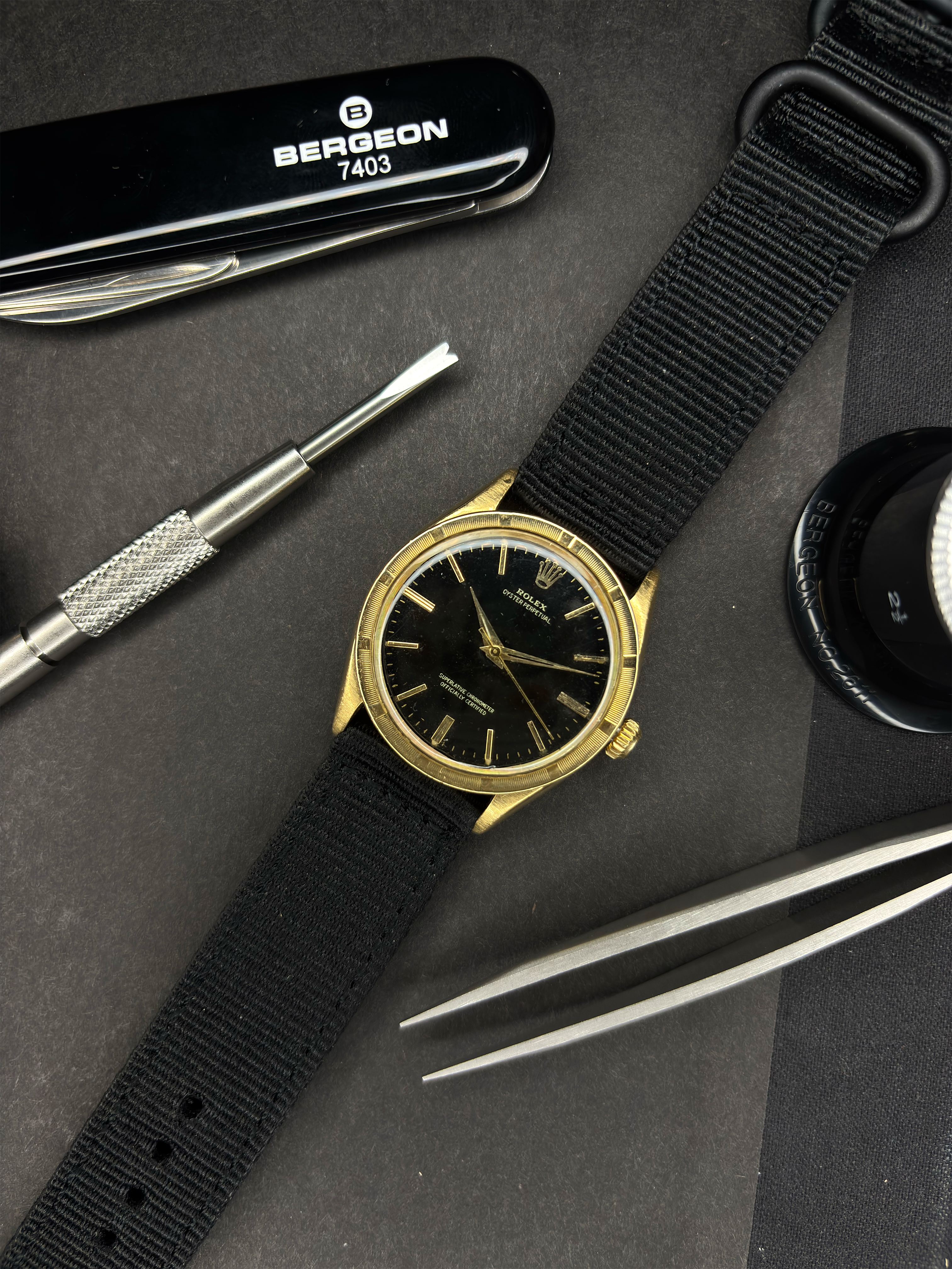 Vintage solid gold Rolex watch with black strap on a dark surface with tools and Bergeon branding.