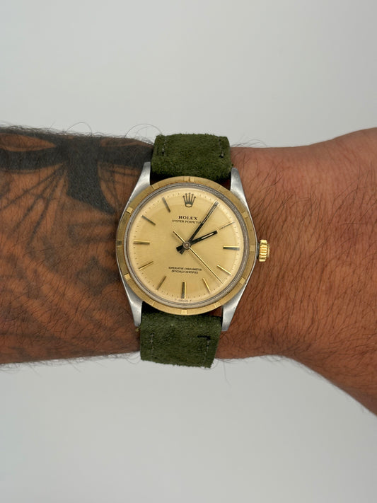 Vintage Rolex watch with a green strap on a wrist against a neutral background