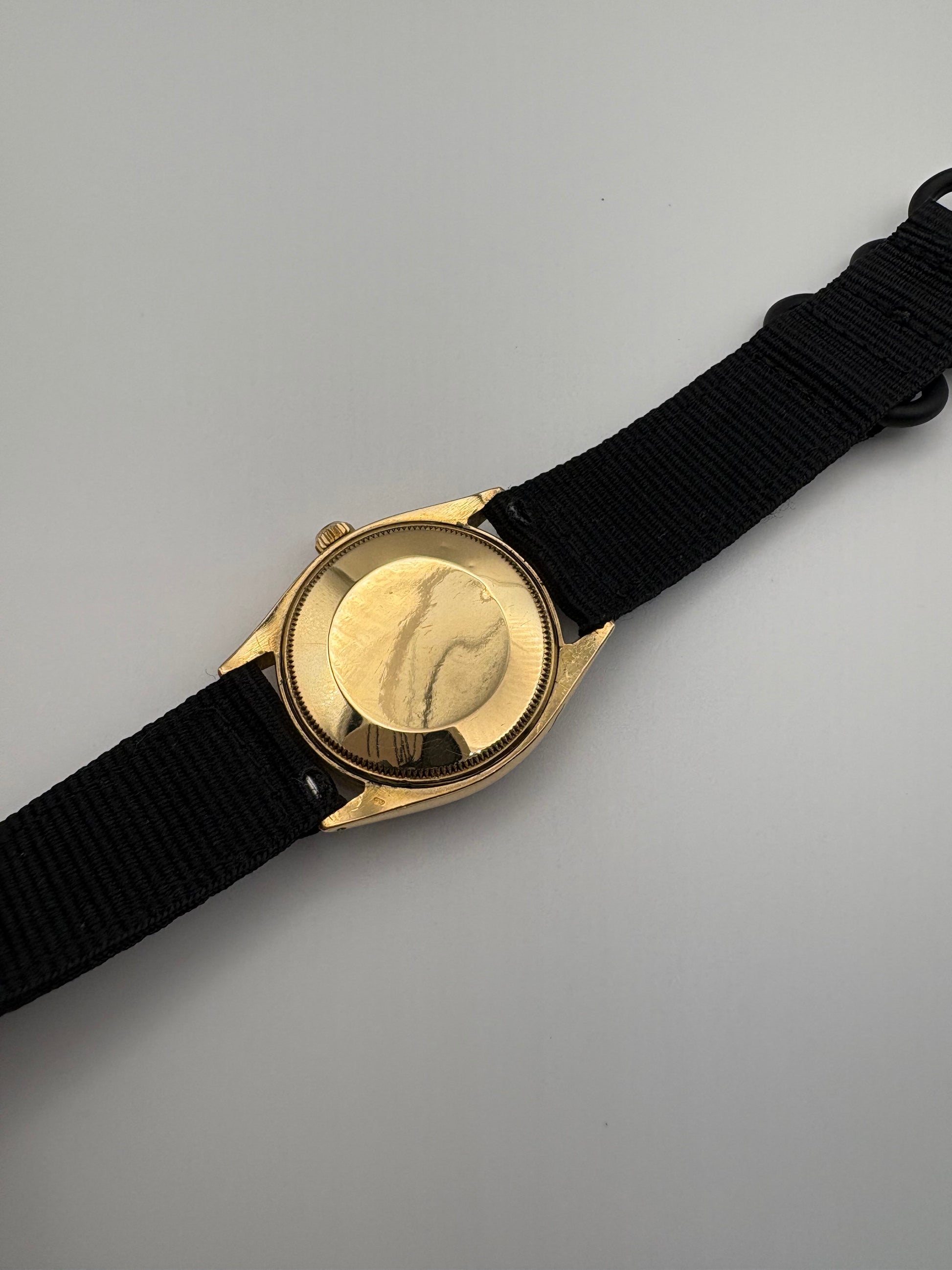 Gold watch casebook with black strap on a gray background