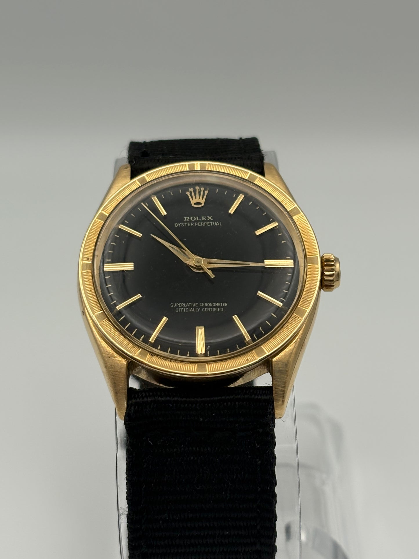 Gold wristwatch with black face and strap on a gray background