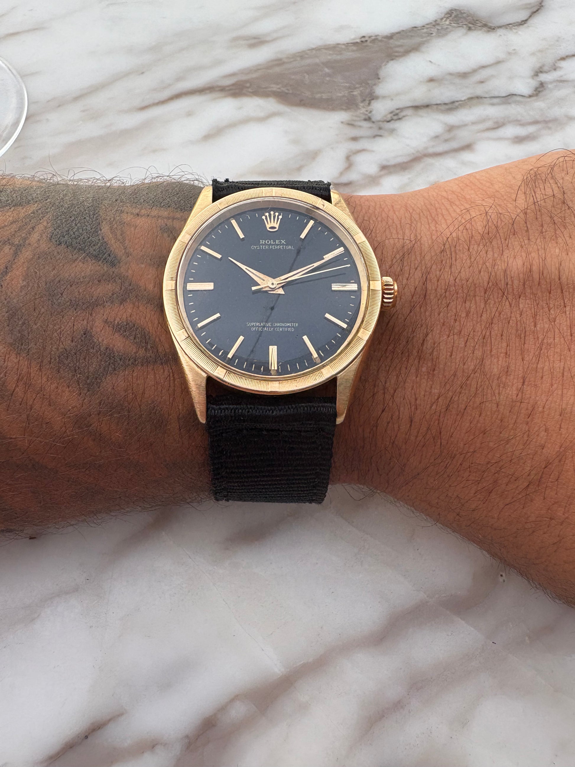 Gold watch with black strap on a wrist against a marble background