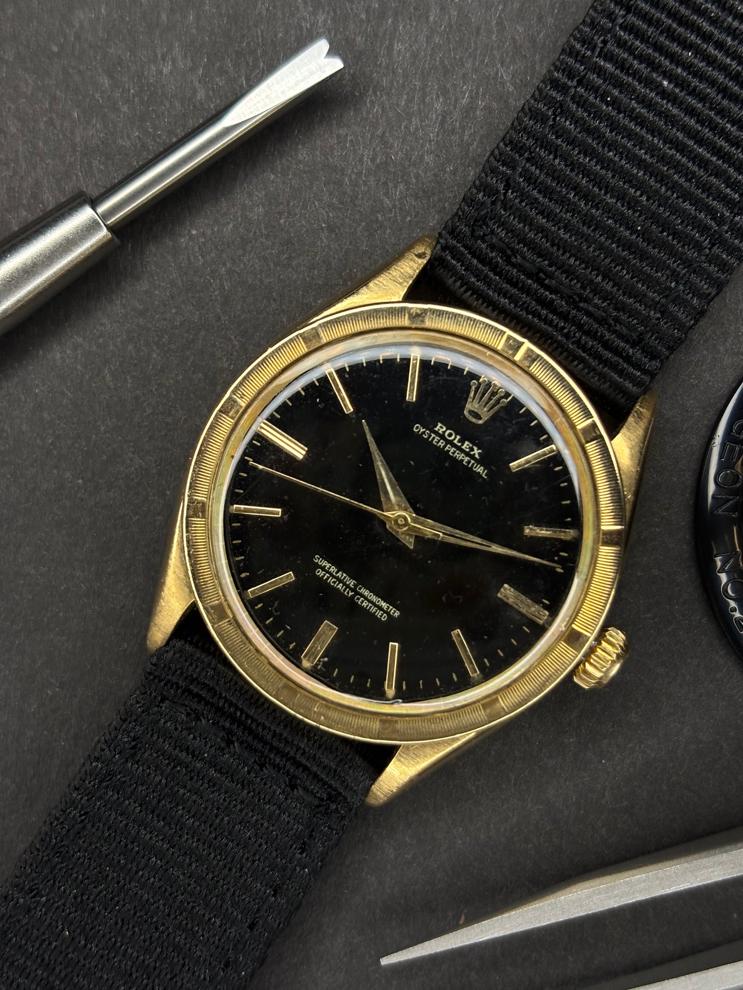 Swiss made mechanical vintage, solid gold vintage Rolex wristwatch with black dial on a dark surface with tools