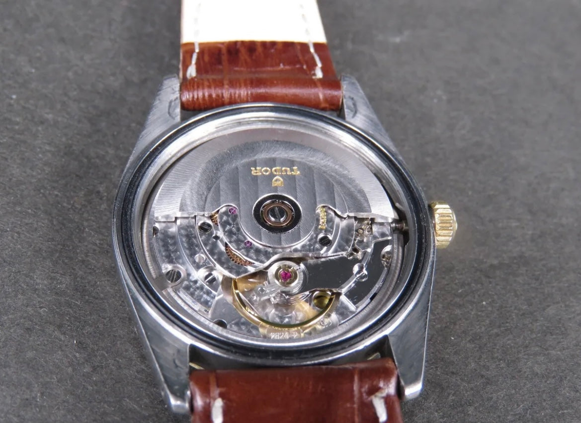 Watch with brown leather strap and visible movement on a gray background
